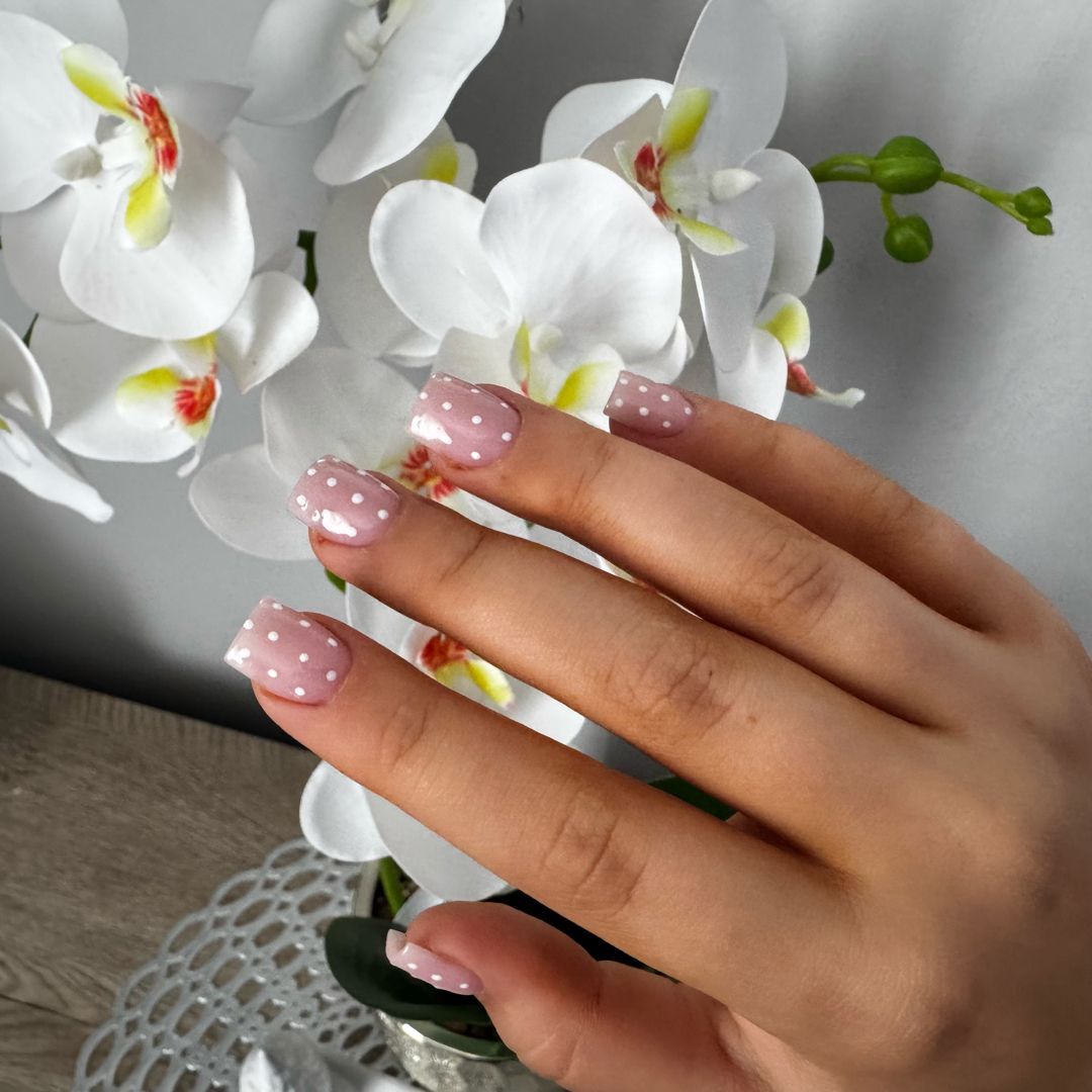 Różowe paznokcie w drobne białe kropki ułożone obok białej orchidei